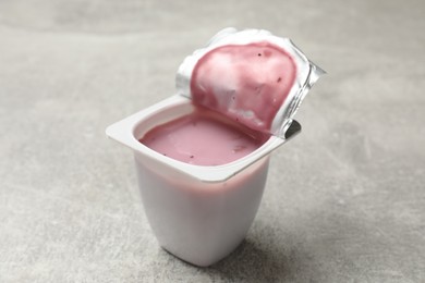 Photo of Delicious yogurt in plastic cup on gray textured table, closeup