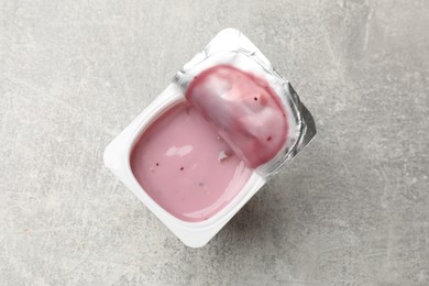 Photo of Delicious yogurt in plastic cup on gray textured table, top view