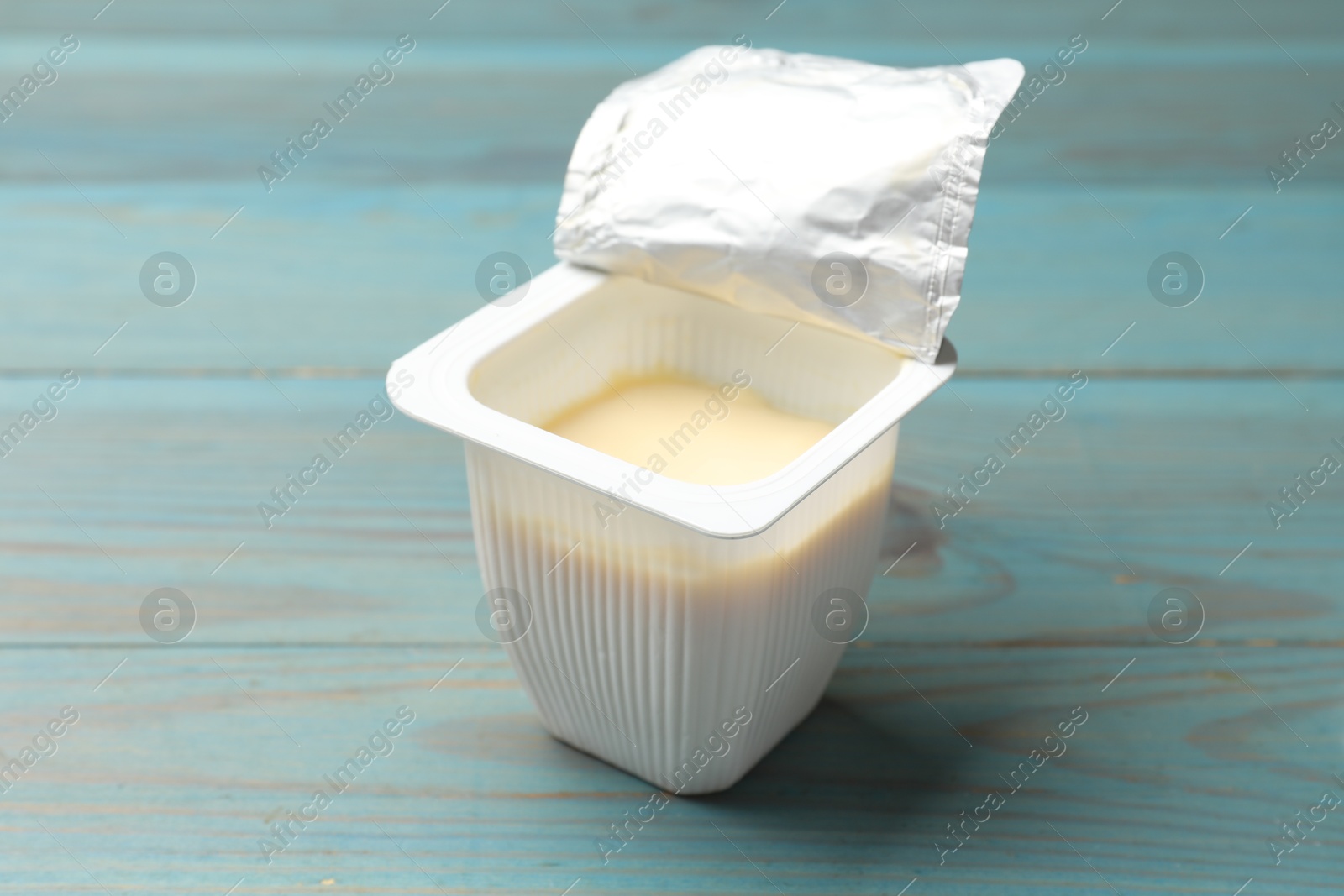 Photo of Delicious yogurt in plastic cup on light blue wooden table, closeup