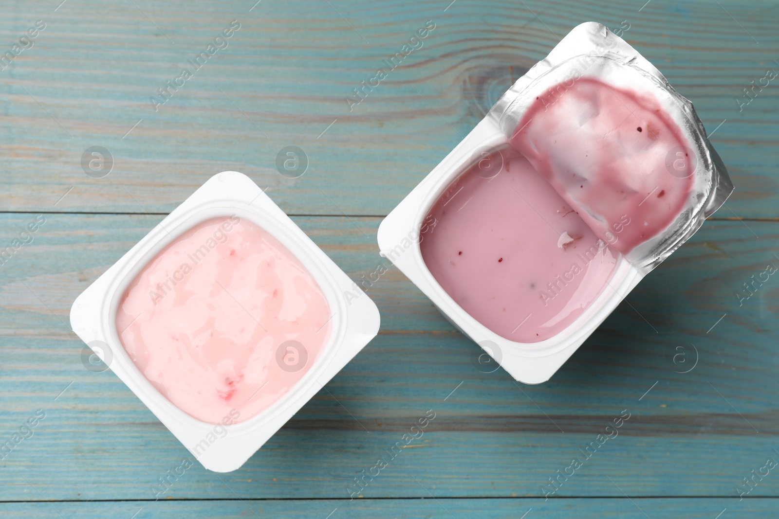 Photo of Delicious yogurts in plastic cups on light blue wooden table, flat lay