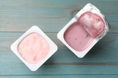 Photo of Delicious yogurts in plastic cups on light blue wooden table, flat lay