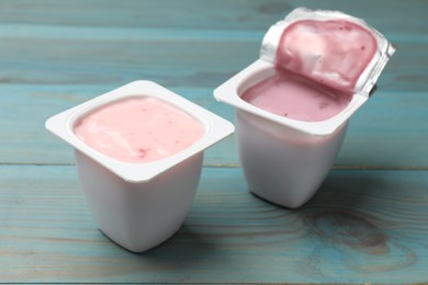 Photo of Delicious yogurts in plastic cups on light blue wooden table, closeup