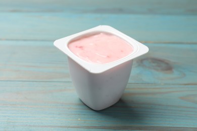 Photo of Delicious yogurt in plastic cup on light blue wooden table, closeup