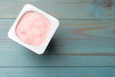 Photo of Delicious yogurt in plastic cup on light blue wooden table, top view. Space for text