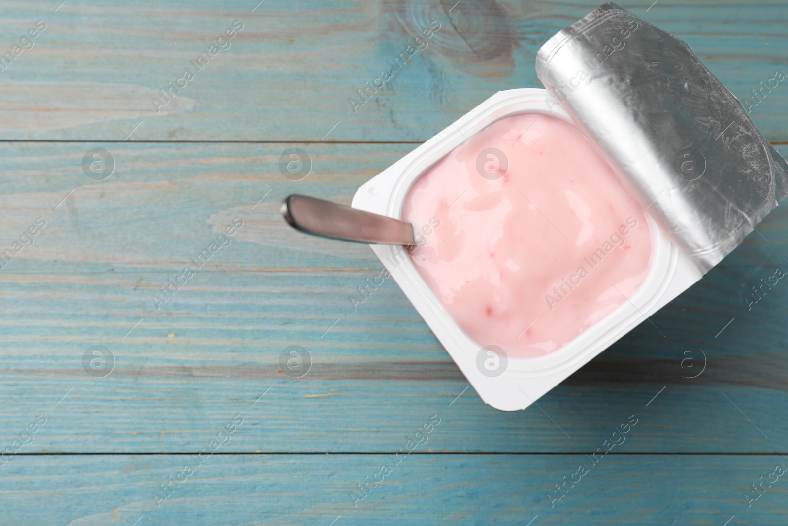 Photo of Delicious yogurt in plastic cup with spoon on light blue wooden table, top view. Space for text