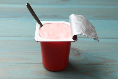 Photo of Delicious yogurt in plastic cup with spoon on light blue wooden table, closeup