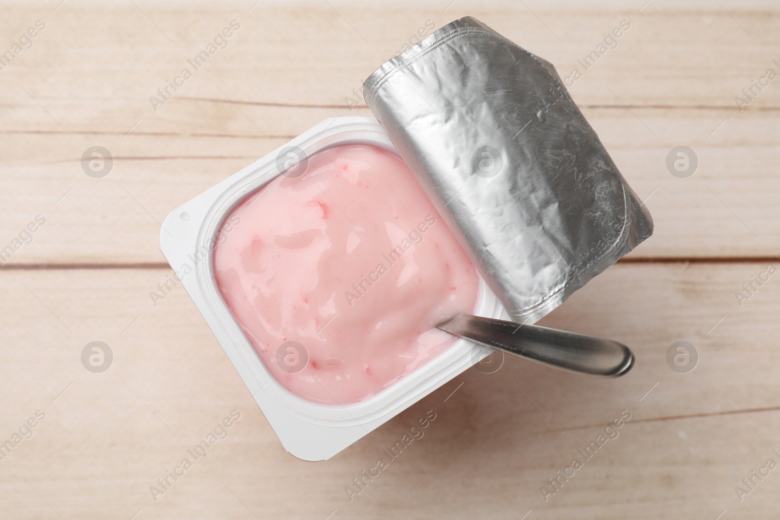 Photo of Delicious yogurt in plastic cup with spoon on wooden table, top view