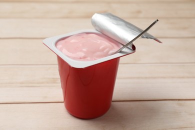 Photo of Delicious yogurt in plastic cup with spoon on wooden table, closeup