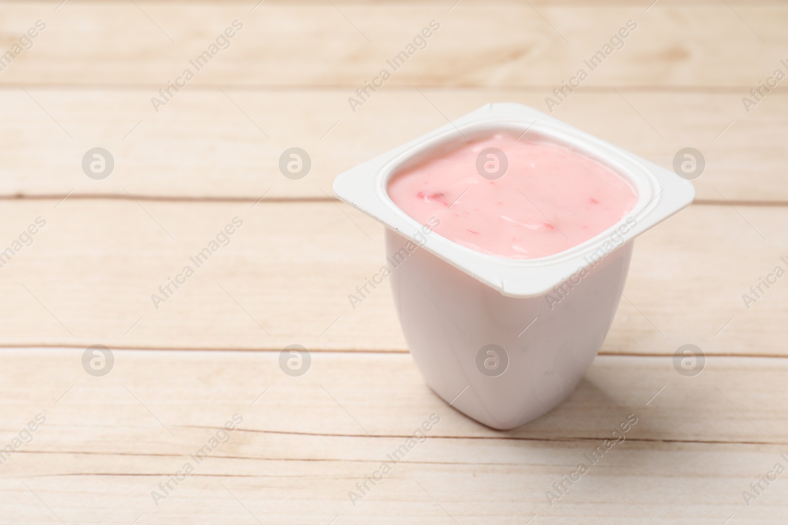 Photo of Delicious yogurt in plastic cup on wooden table, closeup. Space for text