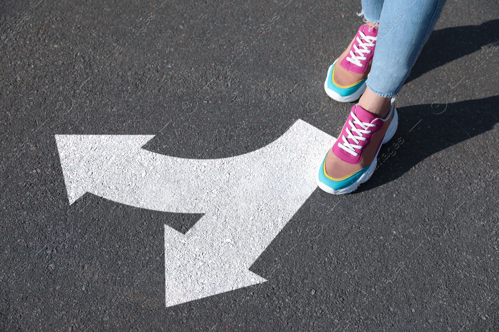 Image of Woman walking toward white arrows pointing in different directions on asphalt road, closeup. Concept of choice and making decisions