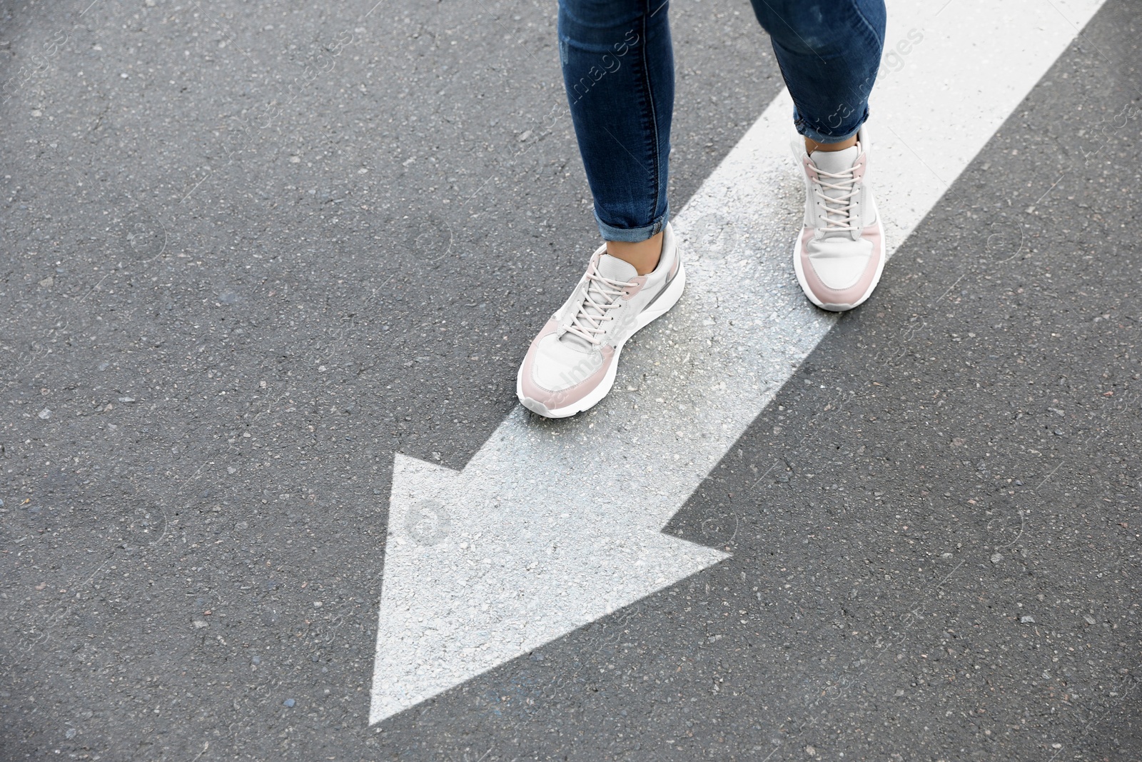 Image of Woman walking on asphalt road with white arrow, closeup. Move forward