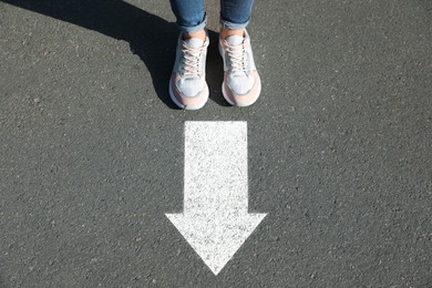 Image of Woman standing near white arrow on asphalt road, closeup. Move forward