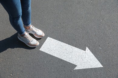 Image of Woman standing near white arrow on asphalt road, closeup. Move forward