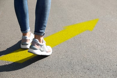 Image of Woman walking on asphalt road with yellow arrow, closeup. Move forward