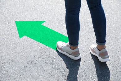 Image of Woman walking toward green arrow on asphalt road, closeup. Move forward