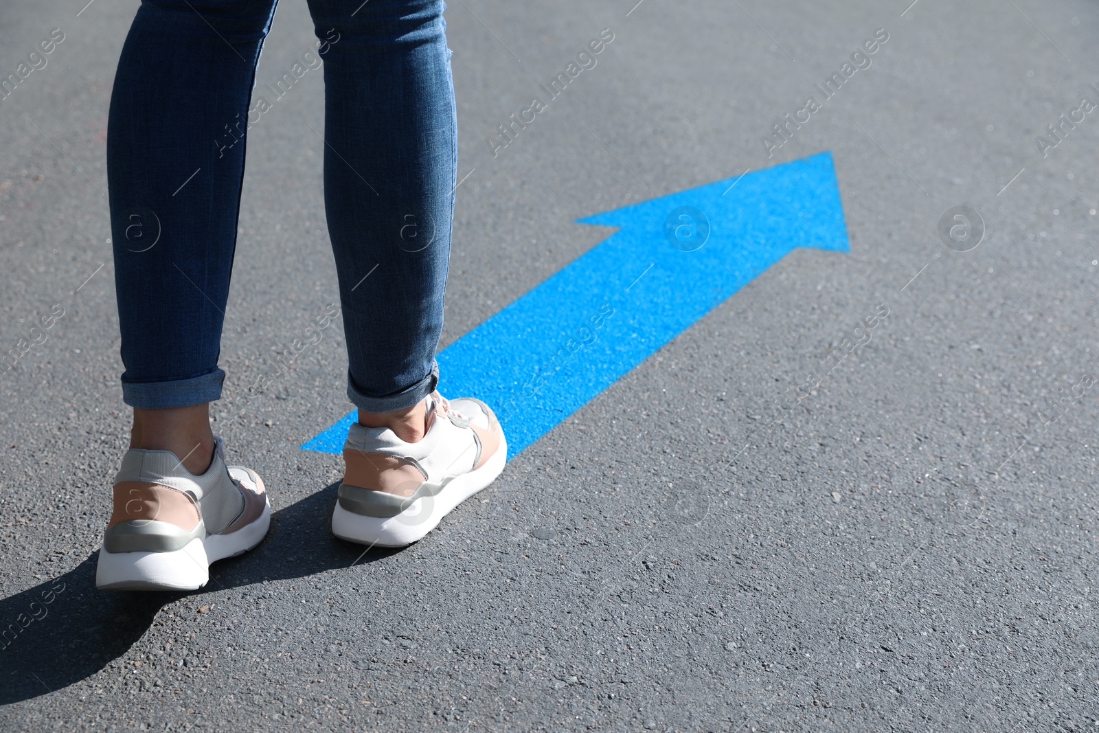 Image of Woman walking toward blue arrow on asphalt road, closeup. Move forward