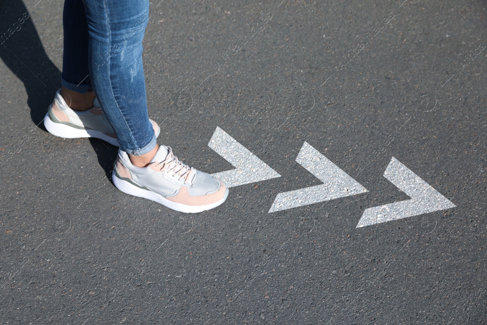 Image of Woman walking toward white arrows on asphalt road, closeup. Move forward