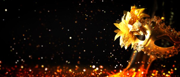 Image of Beautiful carnival mask on black background with golden glitter, bokeh effect. Banner design with space for text