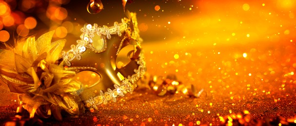 Image of Beautiful carnival mask on golden background with glitter, bokeh effect. Banner design with space for text