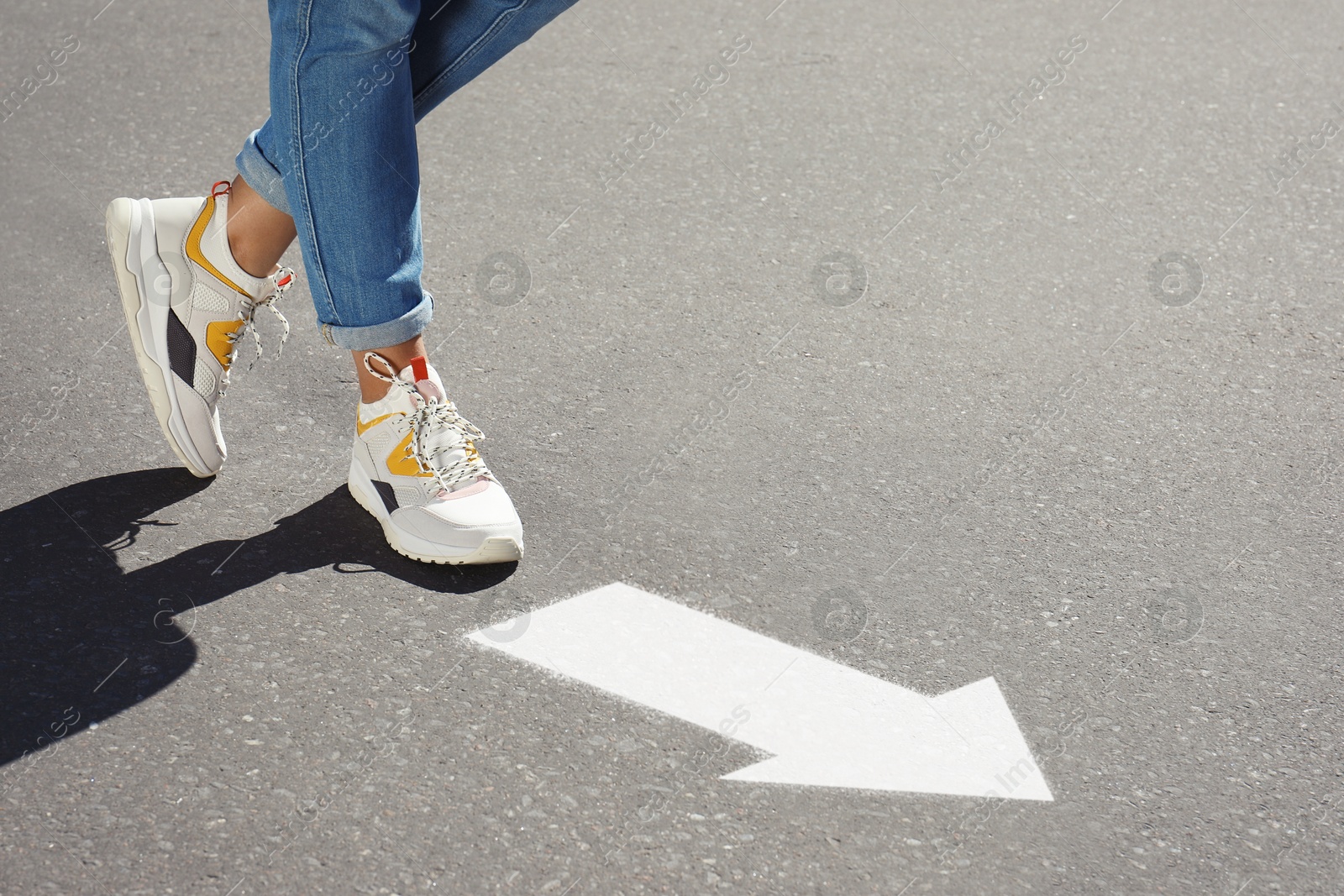 Image of Woman walking toward white arrow on asphalt road, closeup. Move forward