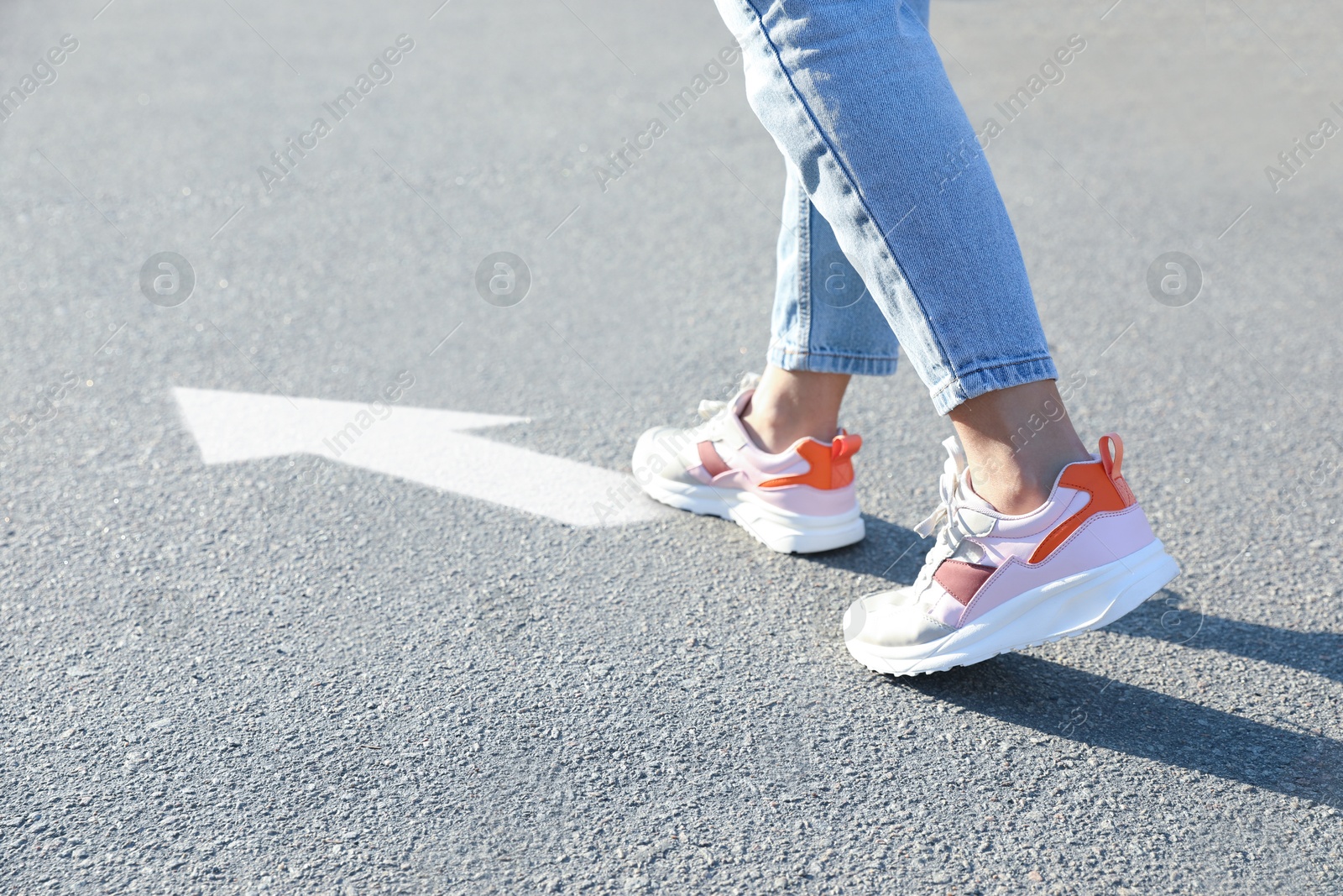 Image of Woman walking toward white arrow on asphalt road, closeup. Move forward