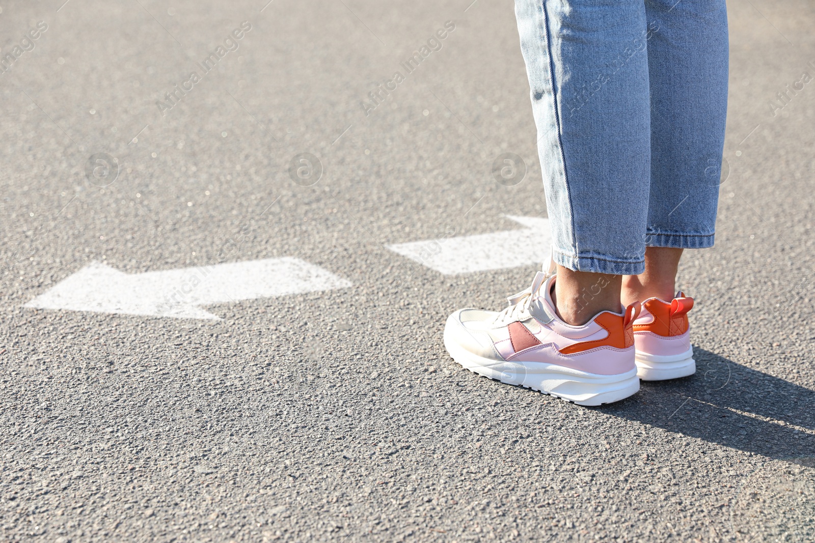 Image of Woman standing near white arrows pointing in different directions on asphalt road, closeup. Concept of choice and making decisions