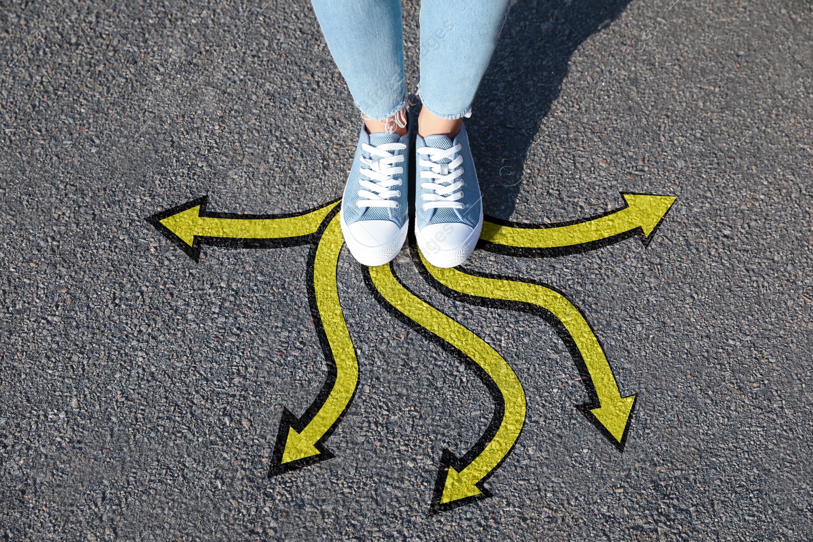 Image of Woman standing on asphalt road with yellow arrows pointing in different directions, top view. Concept of choice and making decisions