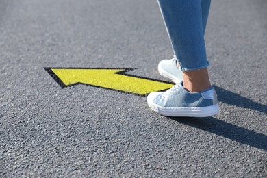 Image of Woman walking toward yellow arrow on asphalt road, closeup. Move forward