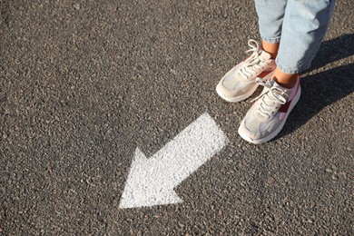 Image of Woman walking toward white arrow on asphalt road, closeup. Move forward