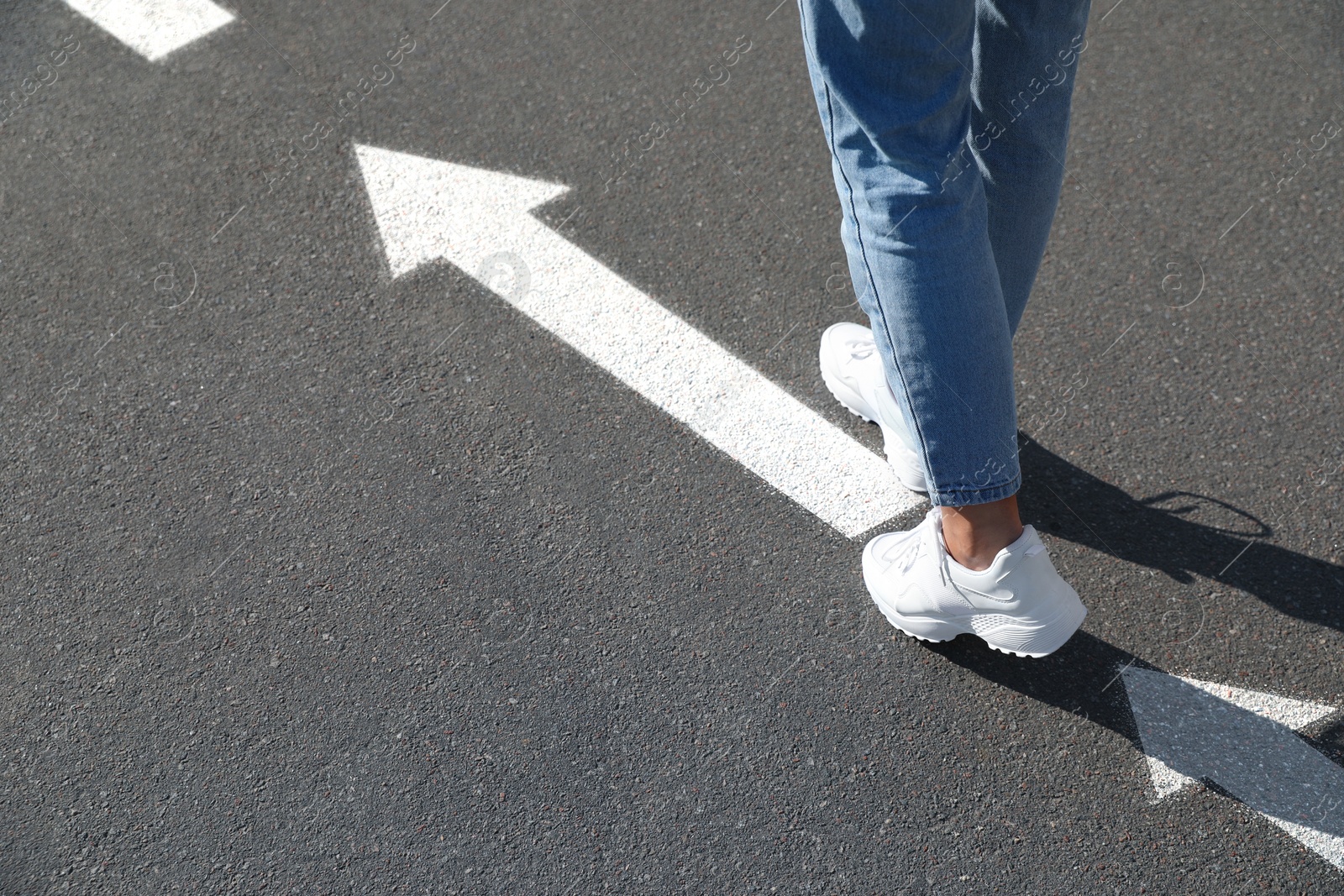 Image of Woman walking on asphalt road with white arrows, closeup. Move forward