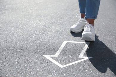 Image of Woman walking toward white arrow on asphalt road, closeup. Move forward