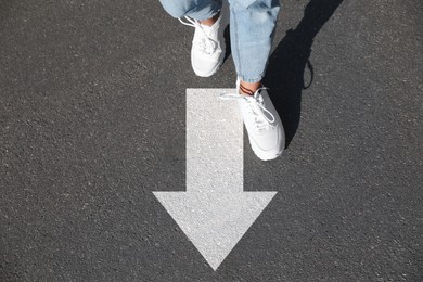 Image of Woman walking toward white arrow on asphalt road, closeup. Move forward