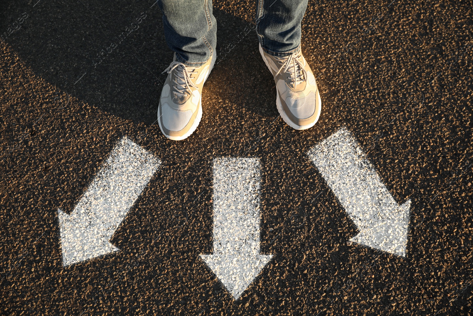 Image of Man standing near white arrows pointing in different directions on asphalt road, top view. Concept of choice and making decisions