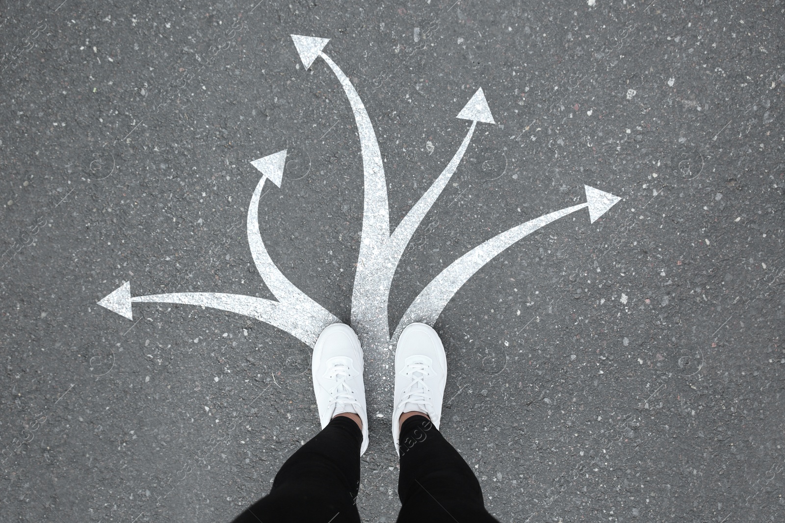 Image of Woman standing on asphalt road with white arrows pointing in different directions, top view. Concept of choice and making decisions