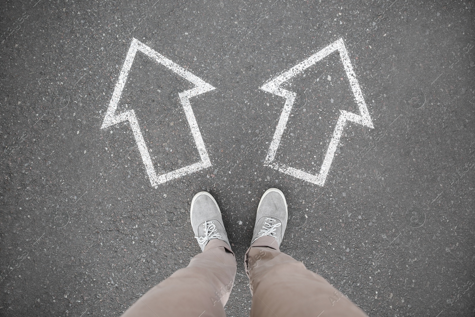 Image of Man standing near white arrows pointing in different directions on asphalt road, top view. Concept of choice and making decisions