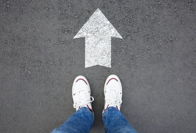 Image of Man standing near white arrow on asphalt road, top view. Move forward