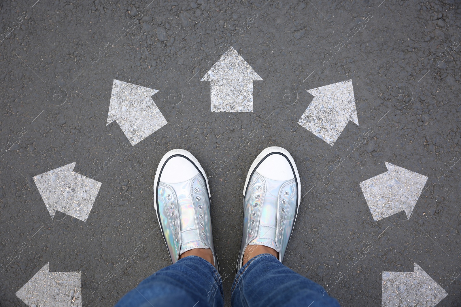 Image of Woman standing near white arrows pointing in different directions on asphalt road, top view. Concept of choice and making decisions