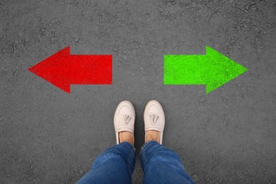 Image of Woman standing near arrows pointing in different directions on asphalt road, top view. Concept of choice and making decisions