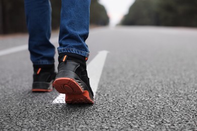 Image of Man walking on asphalt road with white arrow, closeup. Move forward