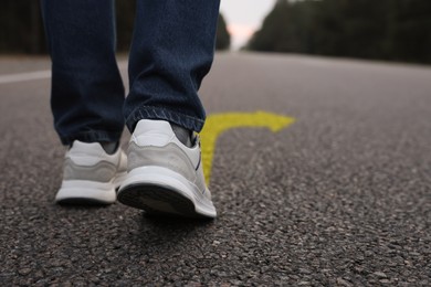 Image of Man walking on asphalt road with yellow arrow, closeup