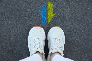 Image of Woman standing near arrows pointing in different directions on asphalt road, top view. Concept of choice and making decisions