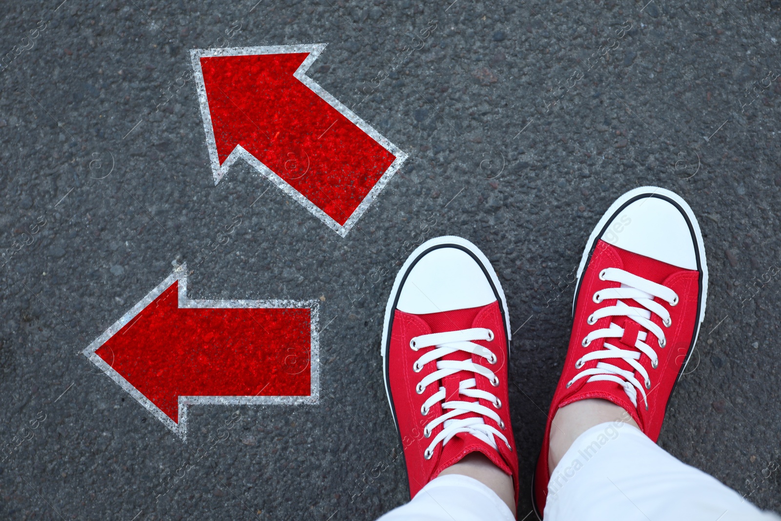 Image of Woman standing near red arrows pointing in different directions on asphalt road, top view. Concept of choice and making decisions