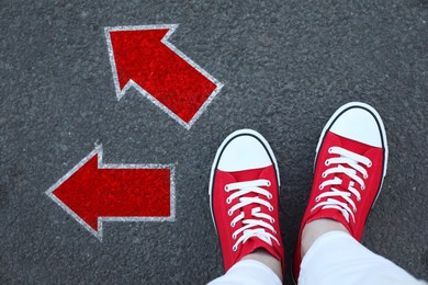 Image of Woman standing near red arrows pointing in different directions on asphalt road, top view. Concept of choice and making decisions