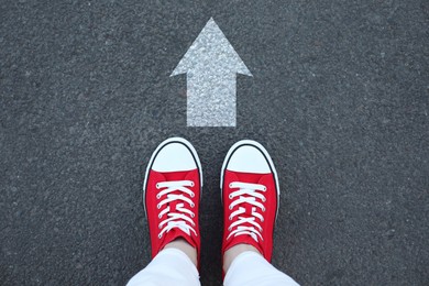 Image of Woman standing near white arrow on asphalt road, top view. Move forward