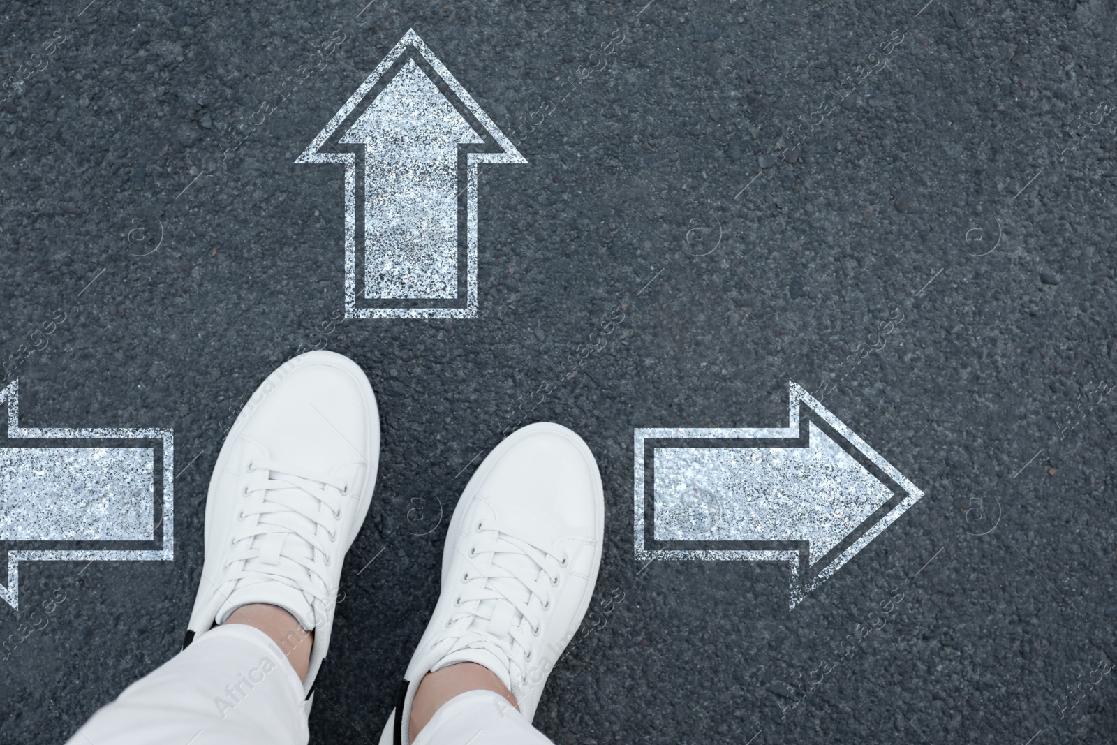 Image of Woman standing near white arrows pointing in different directions on asphalt road, top view. Concept of choice and making decisions