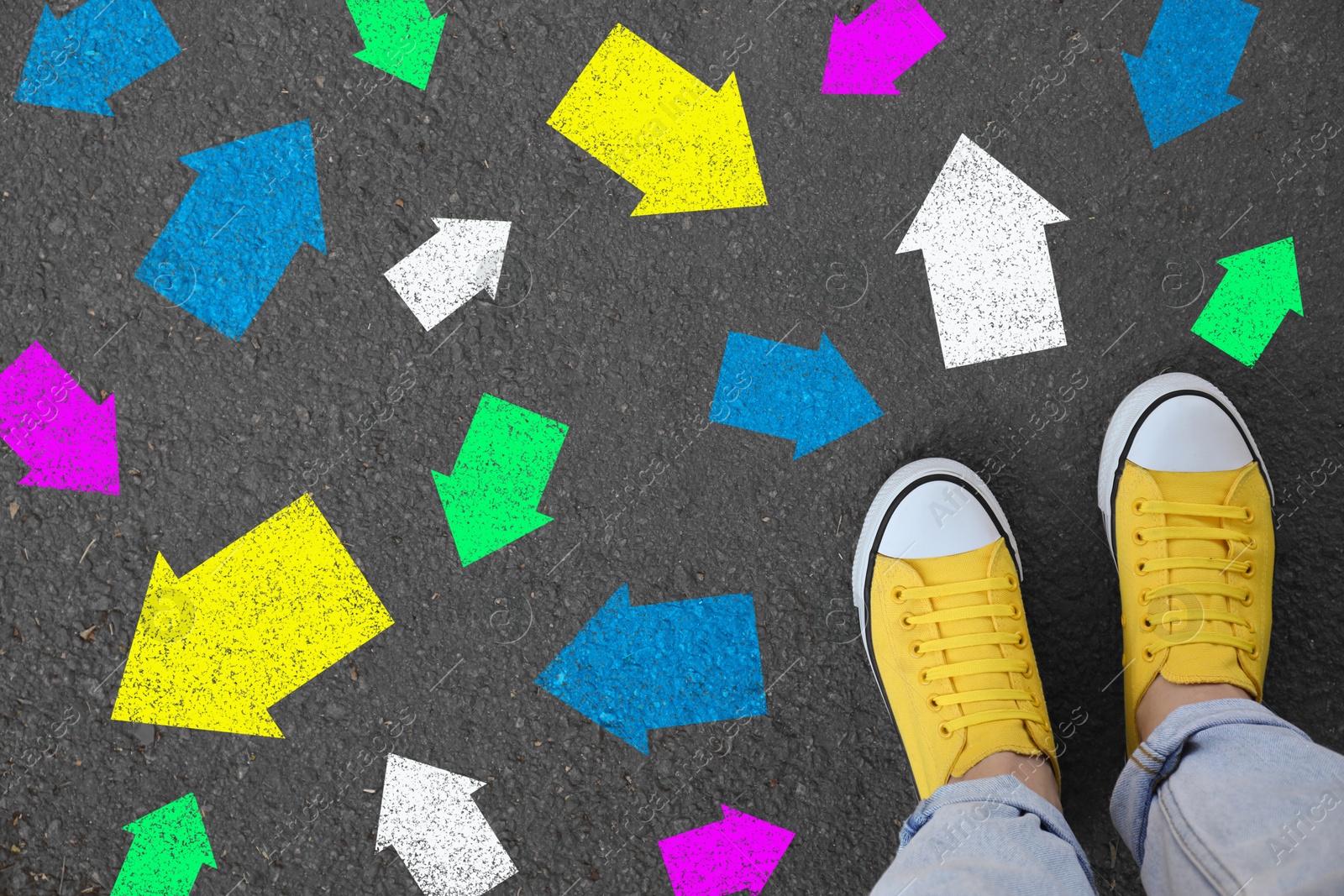 Image of Woman standing on asphalt road with colorful arrows pointing in different directions, top view. Concept of choice and making decisions