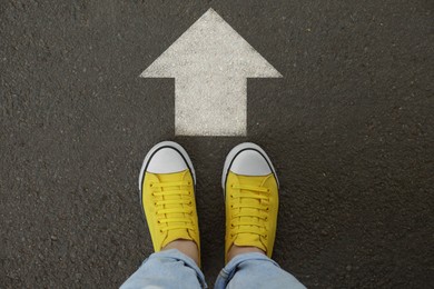 Image of Woman standing near white arrow on asphalt road, top view. Move forward