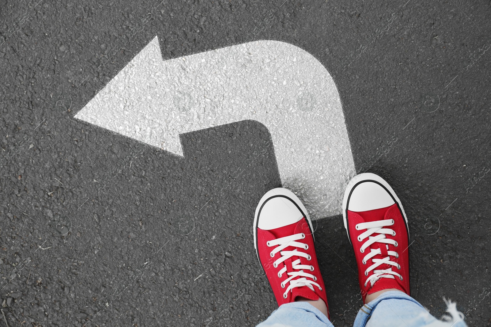 Image of Woman standing on asphalt road with white arrow, top view