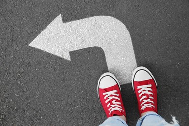 Image of Woman standing on asphalt road with white arrow, top view