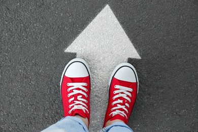 Image of Woman standing on asphalt road with white arrow, top view. Move forward